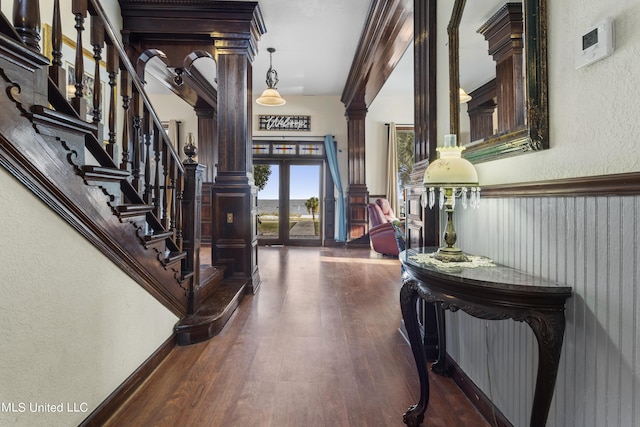foyer entrance featuring a textured wall, dark wood-style flooring, french doors, stairway, and ornate columns