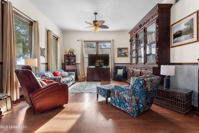 living room featuring wooden walls, wood-type flooring, a textured ceiling, and ceiling fan