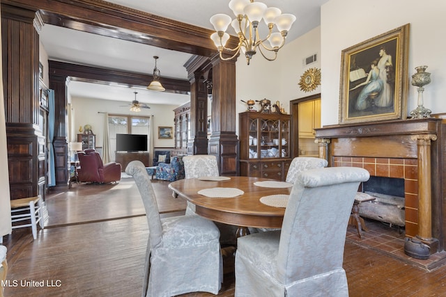 dining room with dark wood finished floors, ceiling fan, a tiled fireplace, a chandelier, and ornate columns