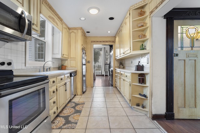 kitchen with appliances with stainless steel finishes, open shelves, a sink, and light countertops