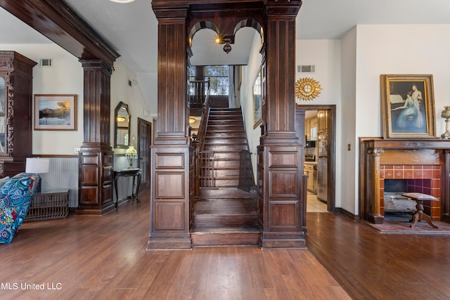 staircase featuring a tiled fireplace, hardwood / wood-style flooring, and decorative columns