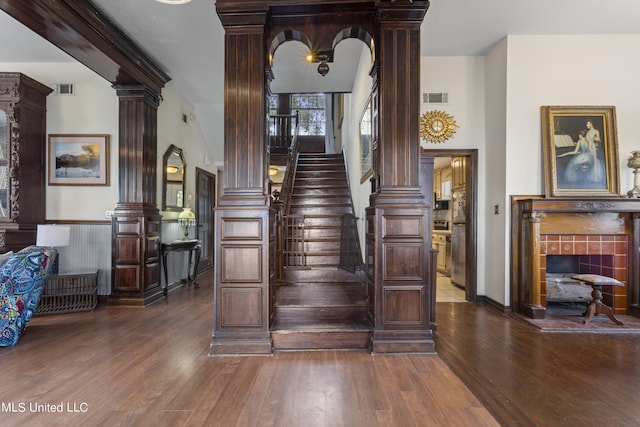 stairs featuring ornate columns, wood finished floors, and a wainscoted wall