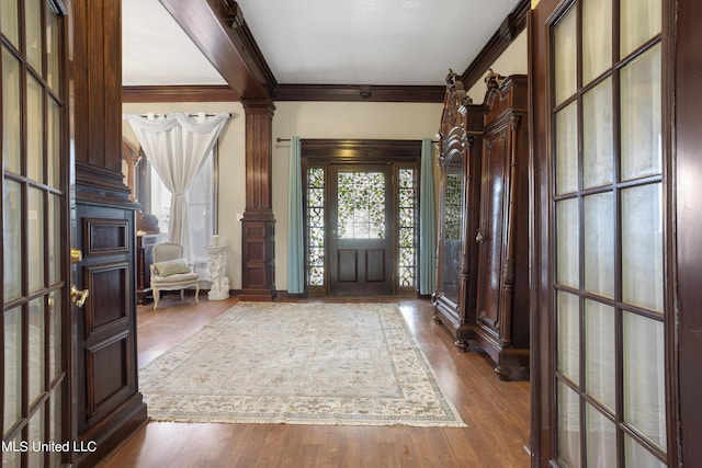 foyer entrance featuring ornamental molding, decorative columns, and wood finished floors
