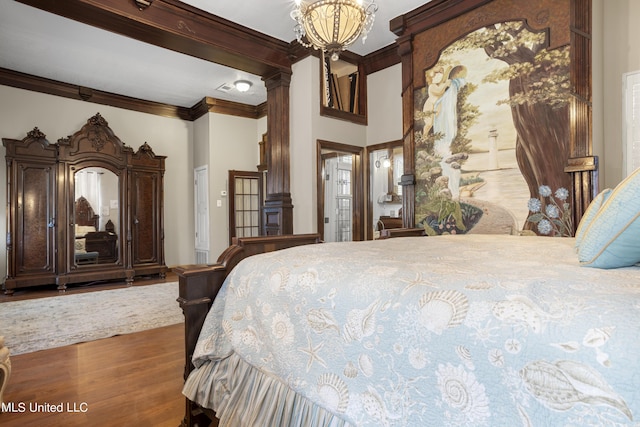 bedroom with crown molding, wood finished floors, decorative columns, and a chandelier