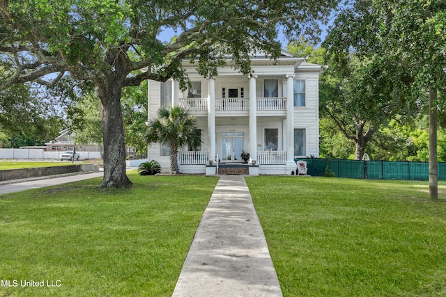 greek revival house featuring a balcony, a front yard, and a porch