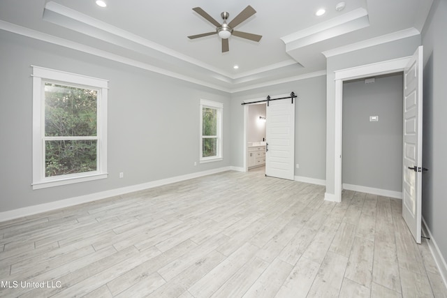 unfurnished bedroom featuring ornamental molding, a barn door, a raised ceiling, light hardwood / wood-style floors, and ceiling fan