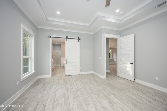 unfurnished bedroom with a raised ceiling, ceiling fan, a barn door, light hardwood / wood-style flooring, and ensuite bath