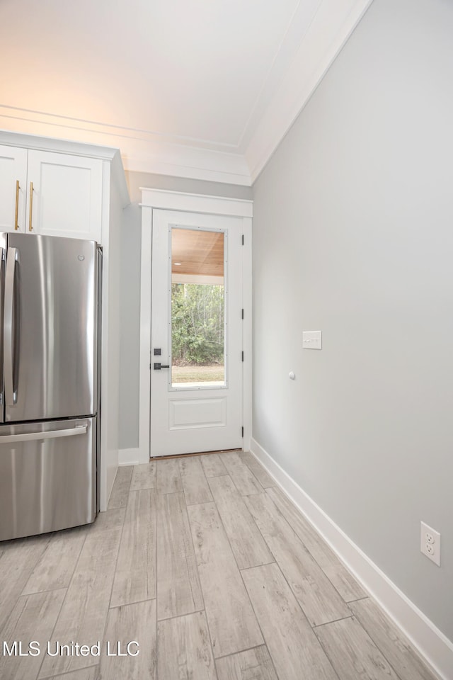 kitchen featuring crown molding, white cabinets, light wood-type flooring, and stainless steel refrigerator