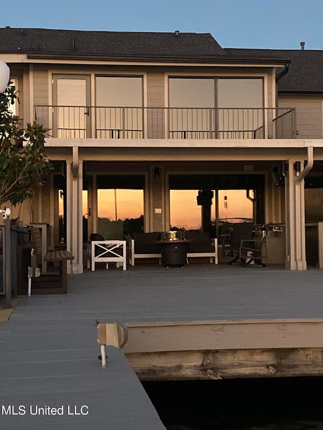 back house at dusk featuring a balcony and an outdoor hangout area