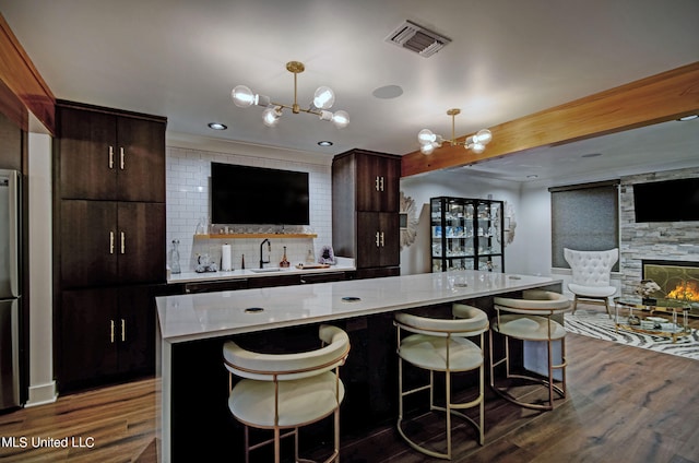 kitchen featuring a kitchen island, a stone fireplace, dark hardwood / wood-style floors, hanging light fixtures, and a notable chandelier