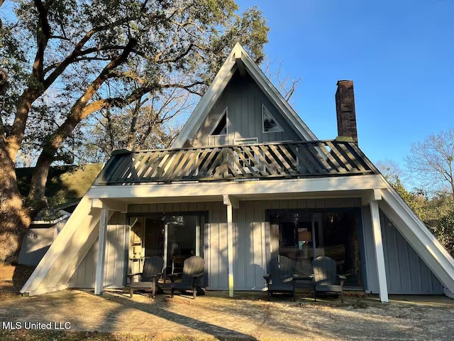 rear view of property featuring a standing seam roof, board and batten siding, a chimney, and a balcony
