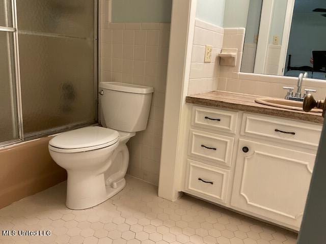 full bathroom featuring toilet, tile patterned flooring, tile walls, bath / shower combo with glass door, and vanity