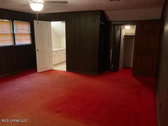 unfurnished bedroom featuring a closet, carpet, ceiling fan, wooden walls, and a textured ceiling