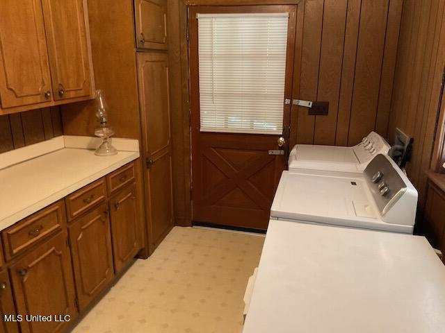 laundry room featuring wooden walls, washing machine and clothes dryer, and cabinets