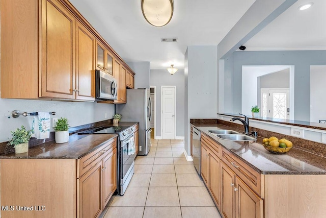 kitchen featuring stainless steel appliances, a sink, light tile patterned floors, a peninsula, and dark stone countertops