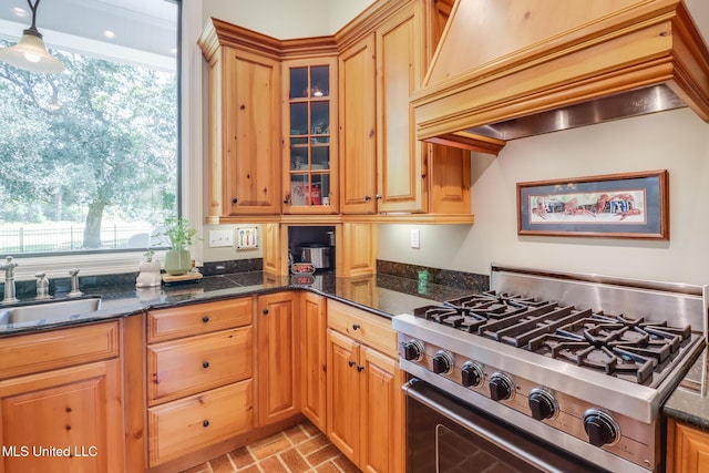kitchen featuring stainless steel gas range oven, a sink, brick patterned flooring, custom exhaust hood, and glass insert cabinets