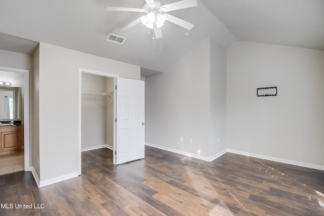 unfurnished bedroom with ensuite bath, dark wood-type flooring, ceiling fan, vaulted ceiling, and a walk in closet