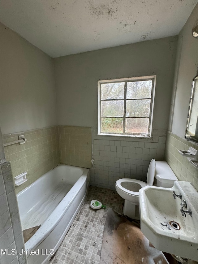 bathroom featuring toilet, sink, tile walls, a tub, and tile patterned flooring