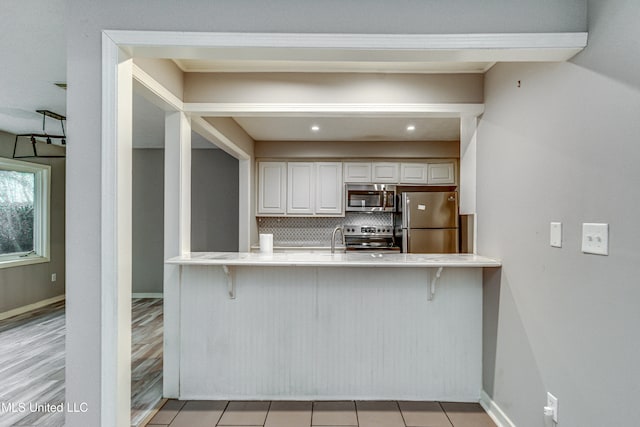 kitchen with tasteful backsplash, appliances with stainless steel finishes, a kitchen bar, and light hardwood / wood-style floors