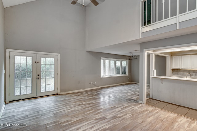 unfurnished living room with french doors, a towering ceiling, light wood-type flooring, sink, and ceiling fan