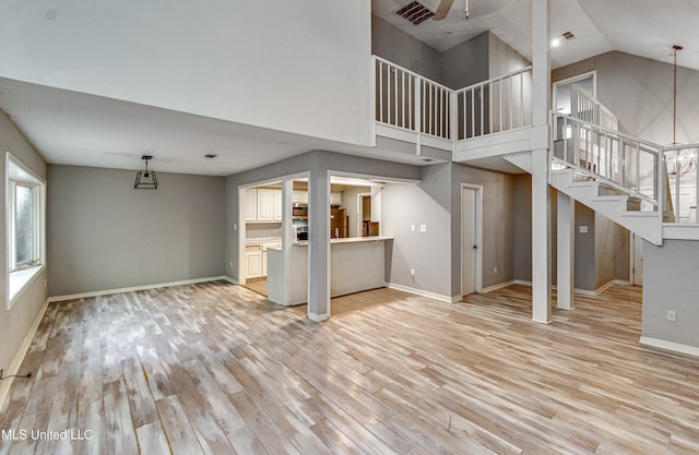 unfurnished living room with a chandelier, light wood-type flooring, and high vaulted ceiling