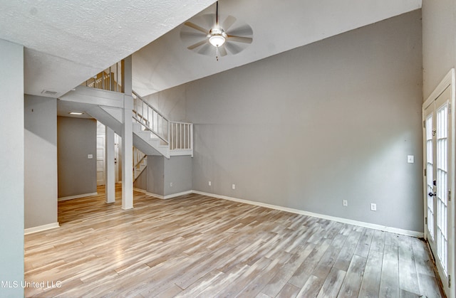 unfurnished living room with light hardwood / wood-style floors, ceiling fan, a towering ceiling, and a textured ceiling