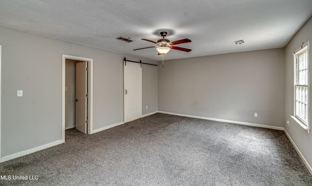 unfurnished bedroom featuring carpet, a barn door, ceiling fan, and a textured ceiling