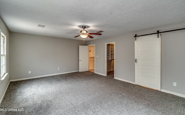 unfurnished bedroom with ceiling fan, a walk in closet, a barn door, a closet, and carpet floors