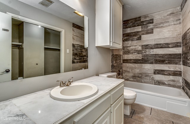 full bathroom with tile patterned floors, vanity, a textured ceiling, tiled shower / bath combo, and toilet