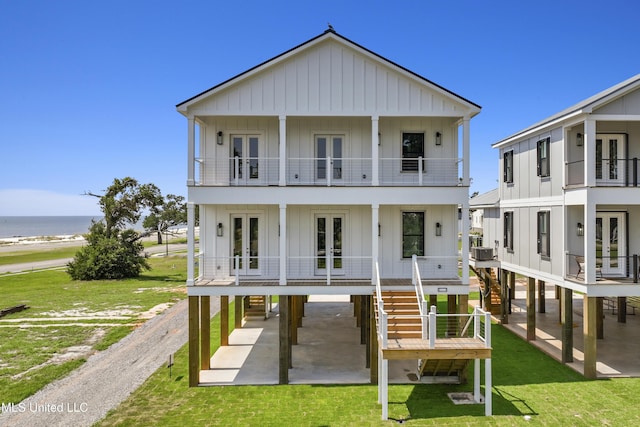 view of front facade with a balcony, driveway, french doors, a front lawn, and board and batten siding