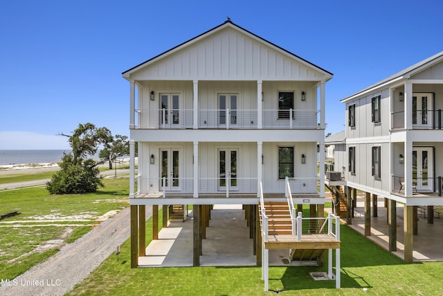 view of front facade with a balcony, driveway, french doors, a front lawn, and board and batten siding