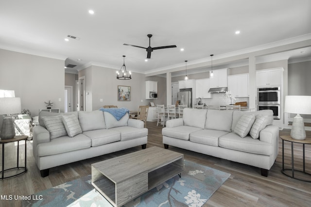 living area with ceiling fan with notable chandelier, crown molding, wood finished floors, and recessed lighting