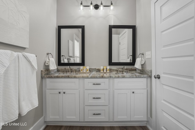 bathroom with double vanity, wood finished floors, a sink, and baseboards