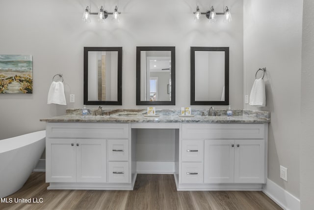 full bath with double vanity, a freestanding tub, a sink, and wood finished floors