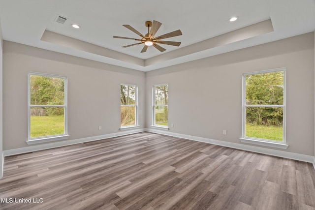 spare room with a tray ceiling, light wood-type flooring, visible vents, and baseboards