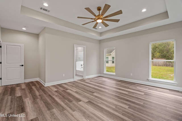 spare room featuring a tray ceiling, wood finished floors, visible vents, and baseboards