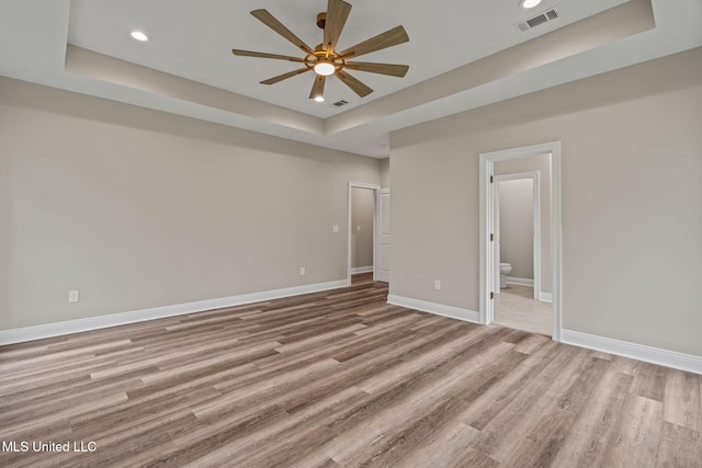 unfurnished bedroom with light wood finished floors, baseboards, visible vents, and a raised ceiling