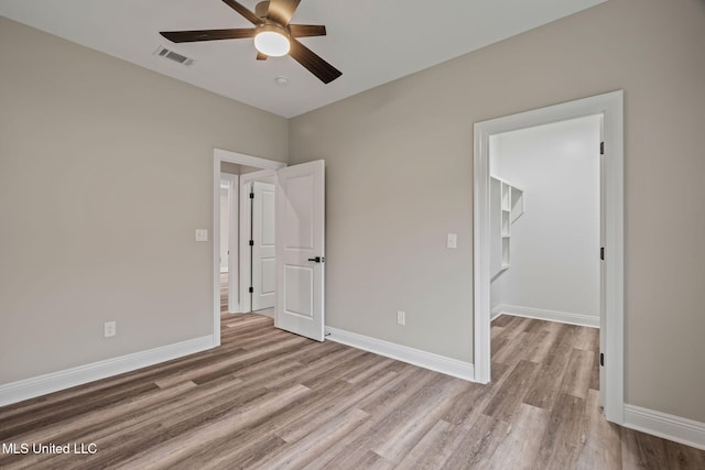 unfurnished bedroom featuring a ceiling fan, visible vents, baseboards, light wood-type flooring, and a walk in closet