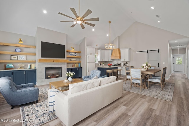 living room featuring visible vents, a glass covered fireplace, ceiling fan, light wood-style floors, and high vaulted ceiling