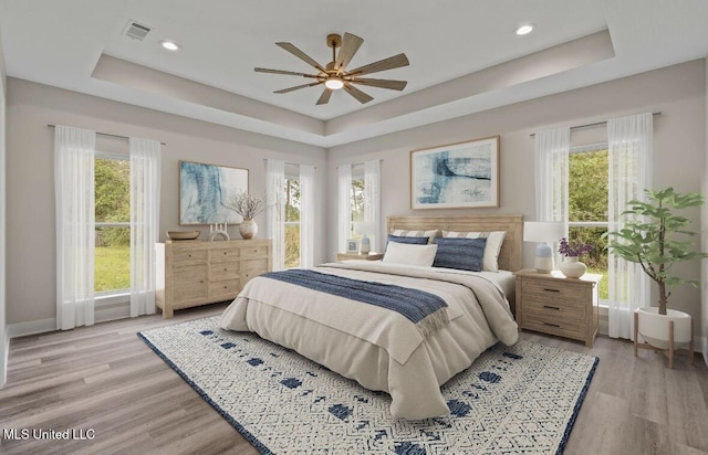 bedroom with a raised ceiling, visible vents, and multiple windows