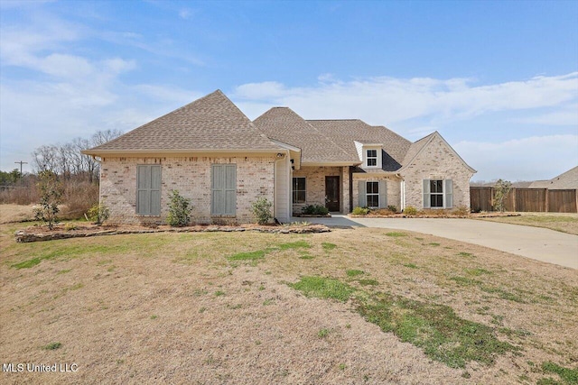 view of front facade with brick siding, fence, a front lawn, and roof with shingles