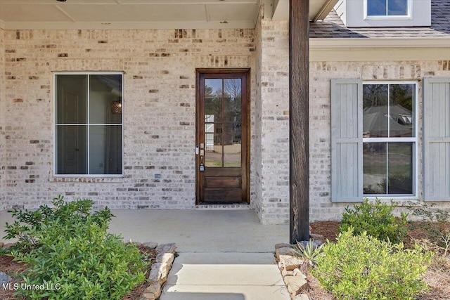 entrance to property featuring a shingled roof and brick siding