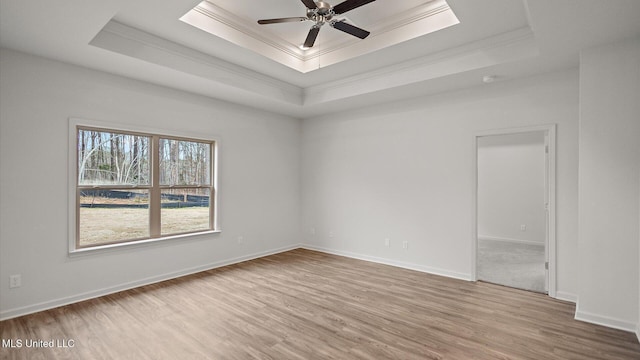 spare room with light hardwood / wood-style flooring, ceiling fan, a skylight, a tray ceiling, and ornamental molding