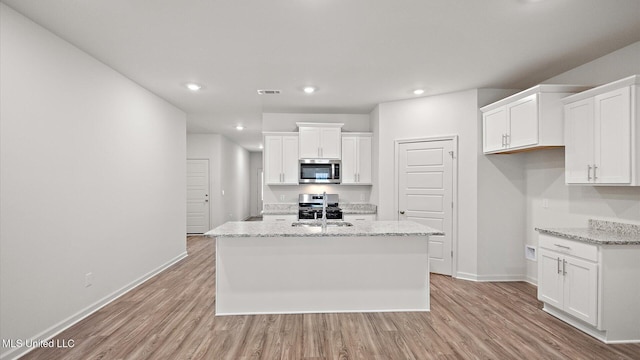 kitchen with white cabinetry, light stone countertops, an island with sink, and appliances with stainless steel finishes