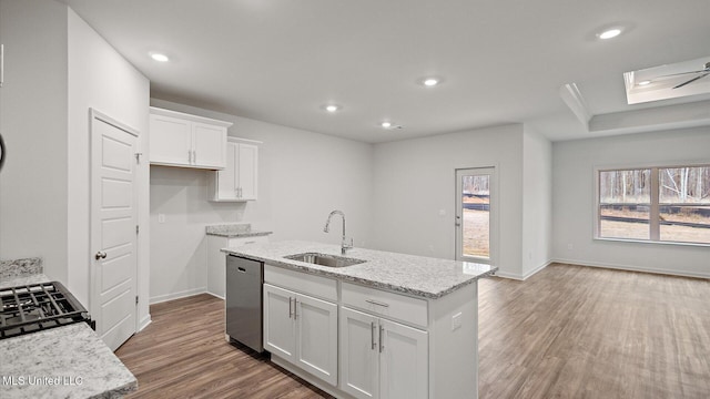 kitchen featuring sink, dishwasher, white cabinetry, light stone counters, and an island with sink