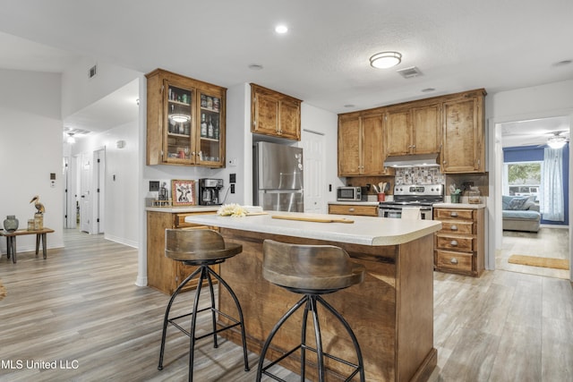 kitchen with a center island, light hardwood / wood-style flooring, appliances with stainless steel finishes, tasteful backsplash, and a breakfast bar area