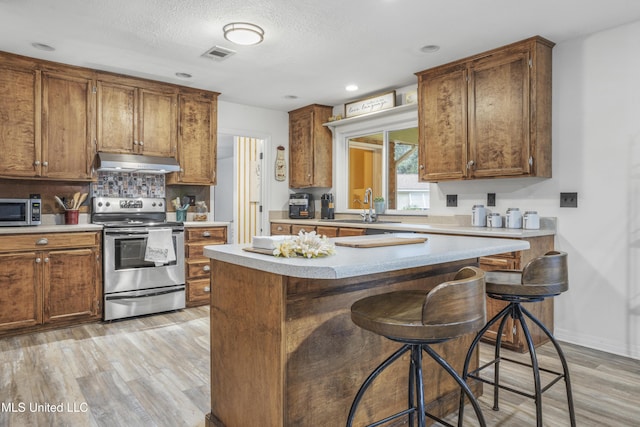 kitchen with a kitchen bar, stainless steel appliances, light hardwood / wood-style floors, and sink