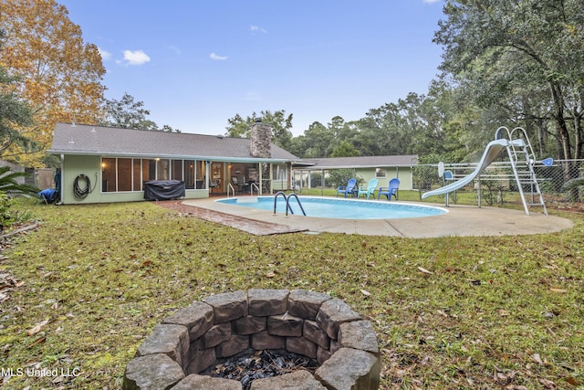 view of swimming pool with a sunroom, a yard, a water slide, and an outdoor fire pit