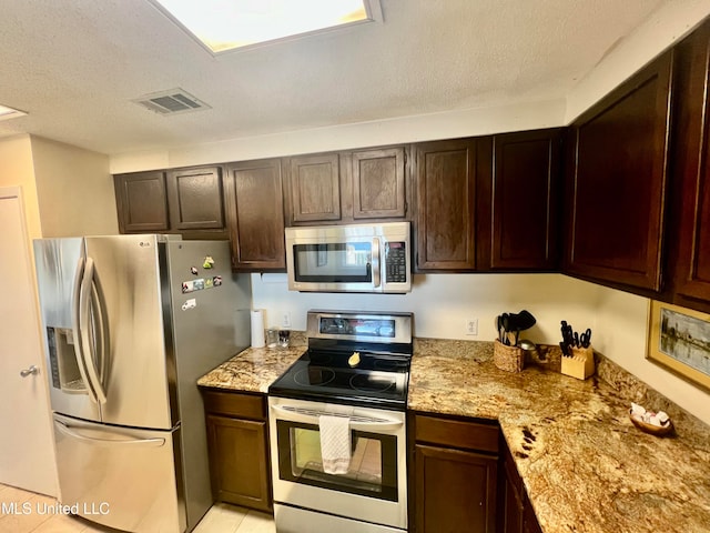 kitchen with a textured ceiling, stainless steel appliances, dark brown cabinetry, light stone counters, and light tile patterned floors