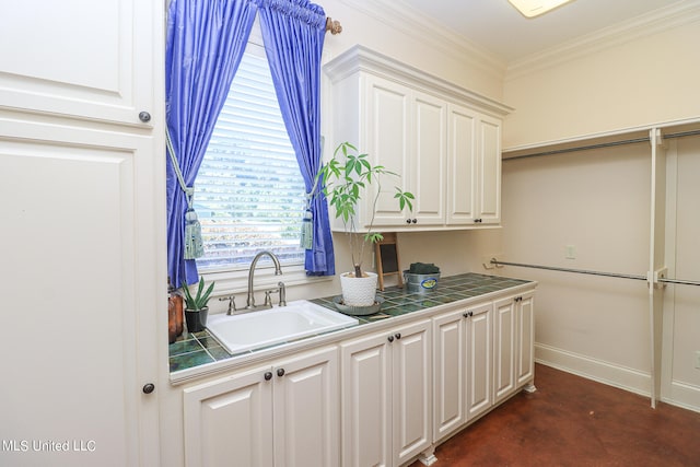 kitchen with tile counters, white cabinets, sink, and crown molding